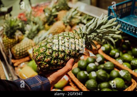 L'uomo sceglie l'ananas - frutta tropicale nel supermercato o nel mercato. Vendita di prodotto sano e gustoso, vitamine. Foto Stock