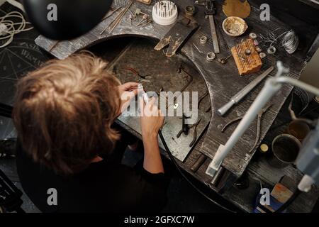 Direttamente al di sopra della vista di produzione di gioielliere utilizzando una macchina abrasiva mentre si fa anello in gioielleria officina Foto Stock