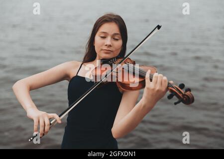 Una ragazza di aspetto asiatico suona il violino in natura. Foto di alta qualità Foto Stock