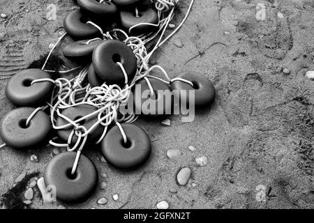 La rete da pesca con galleggianti giace sulla sabbia costiera. Foto in primo piano in bianco e nero con messa a fuoco selettiva Foto Stock