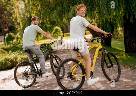 Due bei uomini di vestibilità che cavalcano le loro biciclette in un parco Foto Stock