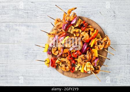 Gamberi Kabobs alla griglia con cipolla rossa, pepe dolce e ananas su un asse di legno, a disposizione piatta Foto Stock