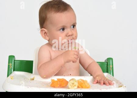 primo piano bambino che sta mangiando frutta in un seggiolone su sfondo bianco Foto Stock