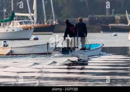 Due uomini e un cane che si dirigono verso l'esterno sullo skiff per lavorare sulla barca di aragosta Maine Foto Stock