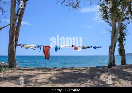 Camper vestiti che asciugano su una linea di lavaggio, tra alberi, vicino al mare su una spiaggia nel sud della Grecia. Foto Stock