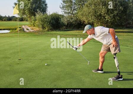 Il golfista professionista con una gamba artificiale durante il gioco del golf punta al bersaglio usando il randello di golf, lunghezza intera Foto Stock