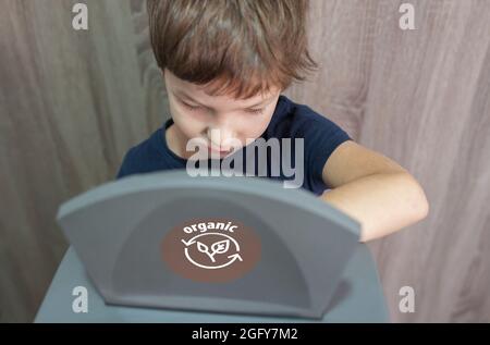 Bambino ragazzo gettando l'articolo organico per lo spreco bidone per biologico a casa. Formazione sul concetto di segregazione dei rifiuti Foto Stock