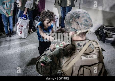 Una Marina statunitense con la 24a unità di spedizione marina (MEU) dà a un bambino una chem light con cui giocare durante un'evacuazione all'aeroporto internazionale Hamid Karzai, Kabul, Afghanistan, 25 agosto. I membri del servizio degli Stati Uniti stanno assistendo il Dipartimento di Stato con un'operazione di evacuazione non combattente (NEO) in Afghanistan. (STATI UNITI Foto del corpo marino di staff Sgt. Victor Mancilla) Foto Stock