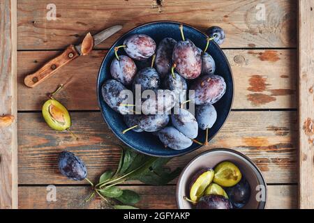 Prugne blu fresche in un recipiente in ceramica. Prugne intere e tagliate a fette. Foto Stock