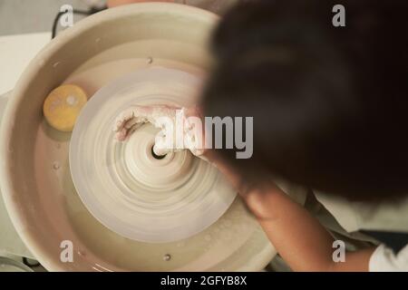 Vista dall'alto di anonimo artigiano femminile che forma il vaso di argilla sulla ruota rotante mentre si artefice di stoviglie in ceramica Foto Stock