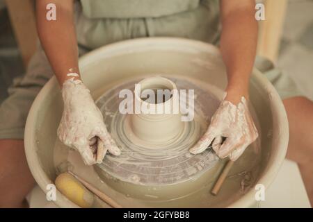 Campione anonimo di raccolto ad angolo alto usando la filettatura speciale per rimuovere il vaso di argilla dalla ruota di ceramica in officina Foto Stock