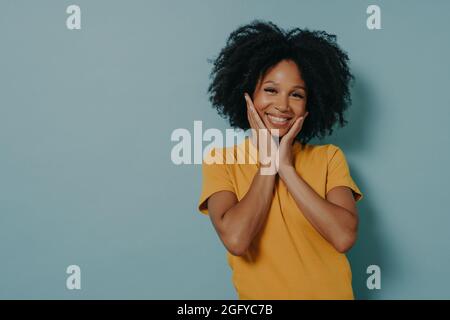 Cute gara mista giovane donna che tocca le guance con le mani e si sente felice dopo aver sentito il complimento Foto Stock