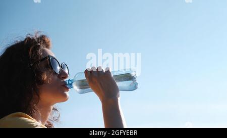 Ragazza con bicchieri beve acqua da una bottiglia in tempo caldo. Foto Stock