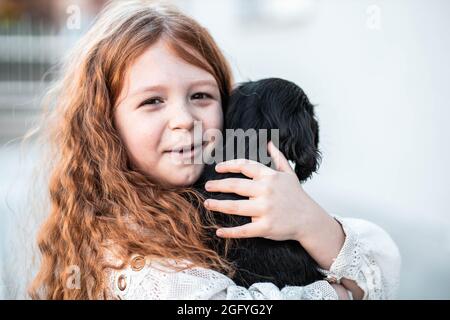 I capelli rossi piccoli frickled ragazza che abbraccia il suo nuovo amico, cucciolo nero carino Foto Stock