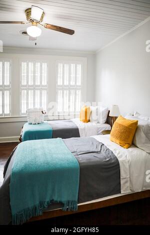 Una camera da letto con due letti singoli con copriletto color turchese e grigio e cuscini decorativi gialli Foto Stock