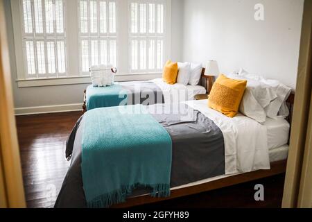Una camera da letto con due letti singoli con copriletto color turchese e grigio e cuscini decorativi gialli Foto Stock