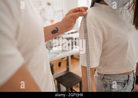 Vista ritagliata del braccio di misurazione del progettista del cliente in maschera medica in studio Foto Stock