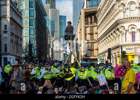 Londra, Regno Unito. 27 agosto 2021. Gli ufficiali di polizia circondano un attivista del clima da Extinction Rebellion che ha eretto ponteggi di bambù durante una protesta che blocca il traffico fuori dalla stazione della metropolitana di Mansion House sulla Queen Victoria Street nella città di Londra. L’evento fa parte della protesta della “rivolta impossibile” di “colpire le cause alla radice della crisi climatica ed ecologica” e rimane in corso per due settimane fino a quando il governo non accetta di fermare tutti i nuovi investimenti di combustibili fossili. Credit: Stephen Chung / Alamy Live News Foto Stock