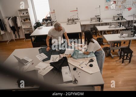 Vista ad angolo alto dei progettisti interrazziali che lavorano vicino a tessuto e schizzi Foto Stock