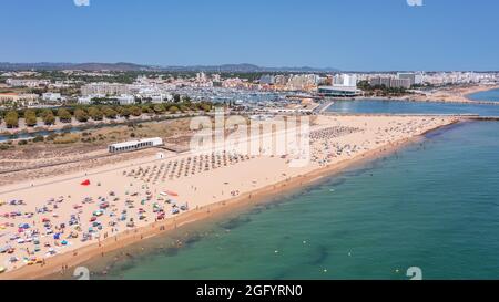 Vista aerea della lussuosa spiaggia di Falesia a Vilamoura. Con i turisti che prendono il sole sui lettini. Porto di Marina con yacht, sullo sfondo. Foto Stock