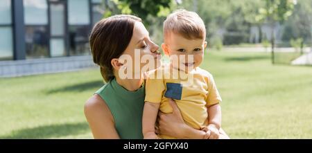 giovane madre baciando felice figlio del bambino fuori, bandiera Foto Stock