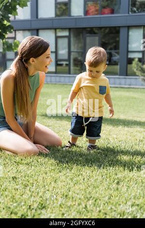 madre eccitata che guarda il figlio del bambino in piedi sull'erba verde Foto Stock