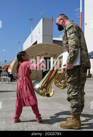 Ramstein Miesenbach, Germania. 24 agosto 2021. Il personale dell'esercito degli Stati Uniti Sgt. William Karsten con l'Army Europe and Africa Band, chiacchiera con un bambino afghano dopo aver suonato musica per intrattenere i rifugiati alla base aerea di Ramstein il 22 agosto 2021 a Ramstein-Miesenbach, Germania. La base aerea di Ramstein fornisce alloggio temporaneo per gli sfollati dall'Afghanistan come parte del Refuge Operation Allees. Credit: Planetpix/Alamy Live News Foto Stock