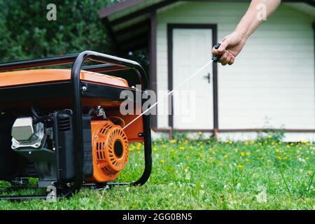 In estate si avvia a mano un generatore elettrico portatile di fronte a una casa estiva Foto Stock