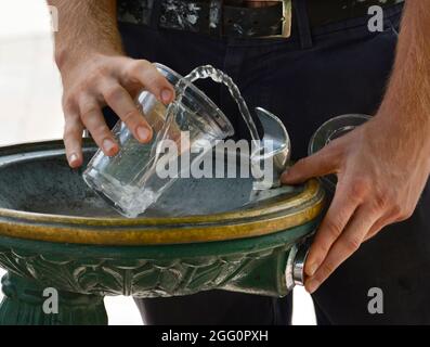 Un uomo riempie un vetro di plastica con acqua presso una fontana pubblica a Santa Fe, New Mexico. Foto Stock