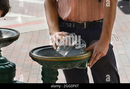 Un uomo riempie un vetro di plastica di acqua da una fontana pubblica bevente a Santa Fe, New Mexico. Foto Stock