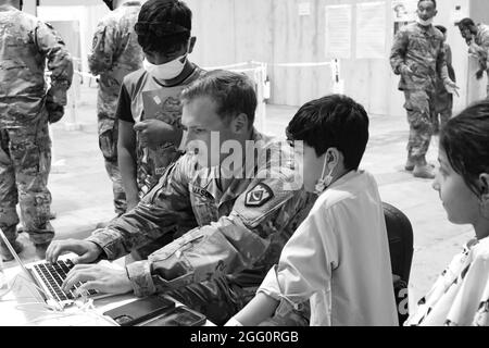 Un soldato della Guardia Nazionale dell'Esercito degli Stati Uniti con la Task Force Spartan, l'Esercito Centrale degli Stati Uniti condivide il suo computer per intrattenere i bambini afghani evacuati a Camp Buehring, Kuwait, 25 agosto 2021. I soldati USARCENT lo hanno colpito rapidamente con i bambini presso la struttura, trovando il modo per portare sorrisi e intrattenere attraverso il processo di arrivo. (STATI UNITI Esercito foto di PFC. Katelynn Bissell) Foto Stock