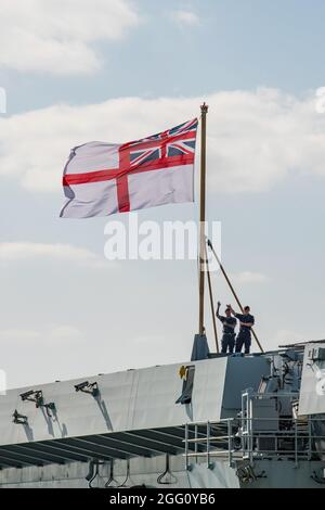 Due marinai della Royal Navy che ondeggiavano sotto la White Ensign sulla portaerei HMS Prince of Wales mentre entra nel porto di Portsmouth, Regno Unito, il 26/8/2021. Foto Stock