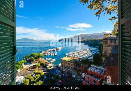 Vista attraverso una finestra aperta con le persiane della baia, del porto, del porticciolo e della colorata città di Sorrento Italia, da una terrazza che si affaccia sul Mediterraneo Foto Stock