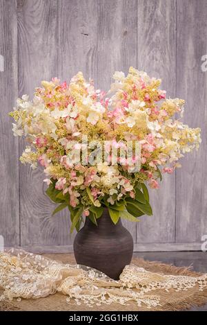 Bouquet di bianco con spruzzi rosa di hydrangeas in un vaso sul tavolo contro lo sfondo di un muro di legno. Foto Stock