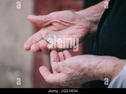 Primo piano le mani stropicciate di una donna anziana contando le monete rimaste in mano Foto Stock