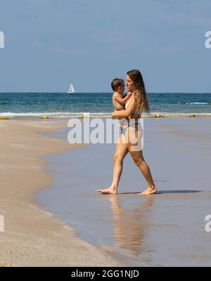 Tel Aviv, Israele - 15 agosto 2021: Una giovane madre con il bambino fra le braccia, sulla spiaggia di Tel Aviv, in una giornata limpida e soleggiata. Foto Stock