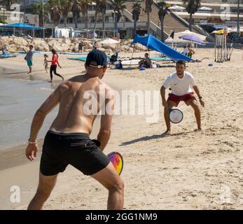 Tel Aviv, Israele - 15 agosto 2021: Due giovani uomini che giocano a matkot sulla spiaggia di Tel Aviv, Israele, in una giornata limpida e soleggiata. Foto Stock