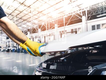 Mano del tecnico che tira verso l'alto il cofano dell'automobile per la manutenzione nell'officina di riparazione Foto Stock