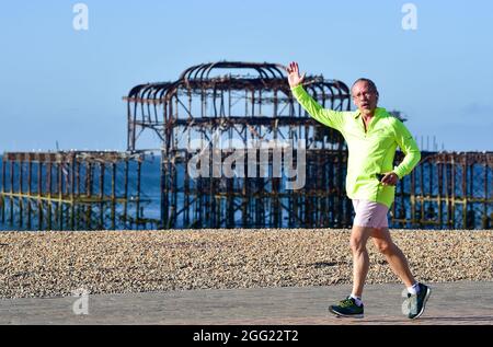 Brighton UK 28 agosto 2021 - un corridore di prima mattina passa dal Molo occidentale di Brighton in luce solare brillante come il tempo è previsto per essere buono per la festa della banca di agosto: Credit Simon Dack / Alamy Live News Foto Stock