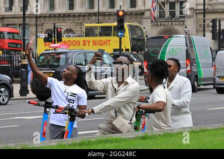 Westminster, Londra, Regno Unito. 27 ago 2021. Quattro giovani uomini scattano foto intorno a Piazza del Parlamento e alle sue numerose attrazioni turistiche mentre esplorano la zona con gli e-scooters. Il centro di Londra sta lentamente tornando ai tempi pre-pandemici, con il numero crescente di visitatori, più visite turistiche, così come più locali che si avventurano in città. Credit: Imagplotter/Alamy Live News Foto Stock