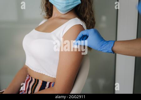 Primo piano del medico in guanti protettivi che tengono la siringa e che usano cotone prima di fare l'iniezione al paziente in maschera medica. Covid-19 o coronavirus Foto Stock