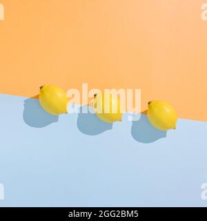 Motivo Liman su sfondo arancione e blu pastello. Composizione minimale estiva alla moda fatta di frutta gialla. Vista dall'alto sulla zona degli agrumi. Foto Stock