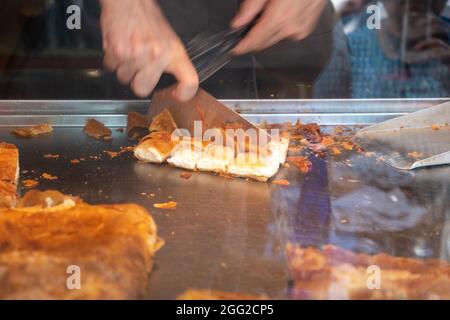 Bougatsa in un negozio, pasticceria da taglio maschile a mano con panna o formaggio a pezzi. Colazione tradizionale con ripieno dolce o salato tra gli strati Foto Stock