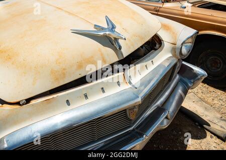 Vista ravvicinata della griglia anteriore arrugginita e del simbolo di un'auto chrysler d'epoca in un cortile esterno con un secondo vecchio veicolo visibile. Foto Stock
