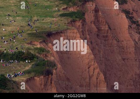 Sidmouth, Devon, Regno Unito. 27 agosto 2021. I membri del pubblico si alzano pericolosamente vicino al bordo di scogliere sbriciolate mentre osservano le frecce rosse della RAF che si esibiscono su Sidmouth, Devon. Le scogliere a Sidmouth sono crollate in questo luogo circa mezza dozzina di volte nelle ultime 4-6 settimane. Credit: Ian Williams/Alamy Live News Foto Stock