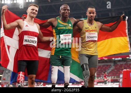 Tokio, Giappone. 28 agosto 2021. Paralimpiadi: Atletica, salto lungo, uomini, finale, allo Stadio Olimpico. I vincitori della medaglia si riuniscono prima della cerimonia di premiazione. La medaglia di bronzo Daniel Wagner dalla Danimarca (l-r), la medaglia d'oro Ntando Mahlingua dal Sudafrica e la medaglia d'argento Leon Schäfer dalla Germania hanno la loro bandiera nazionale nelle loro mani. Credit: Marcus Brandt/dpa/Alamy Live News Foto Stock