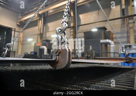 Catene di sollevamento e ganci per il caricamento della lamiera. Posizionamento del metallo su una macchina per il taglio al plasma. Foto Stock