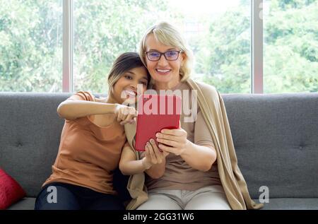 Happy mix pelle famiglia che vivono insieme. Figlia asiatica prendere un selfie con la sua madre caucasica adottata attraverso un computer tablet. Foto Stock