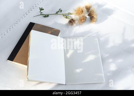 Libro vuoto aperto alla luce del sole. Diario mockup su sfondo tovaglia di lino, lunghe ombre su pagine vuote. Estate matrimonio cancelleria ancora vita scena. Foto Stock