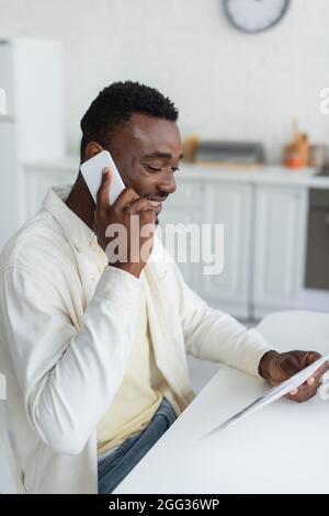 un uomo afro-americano felice che parla su smartphone e legge giornale Foto Stock